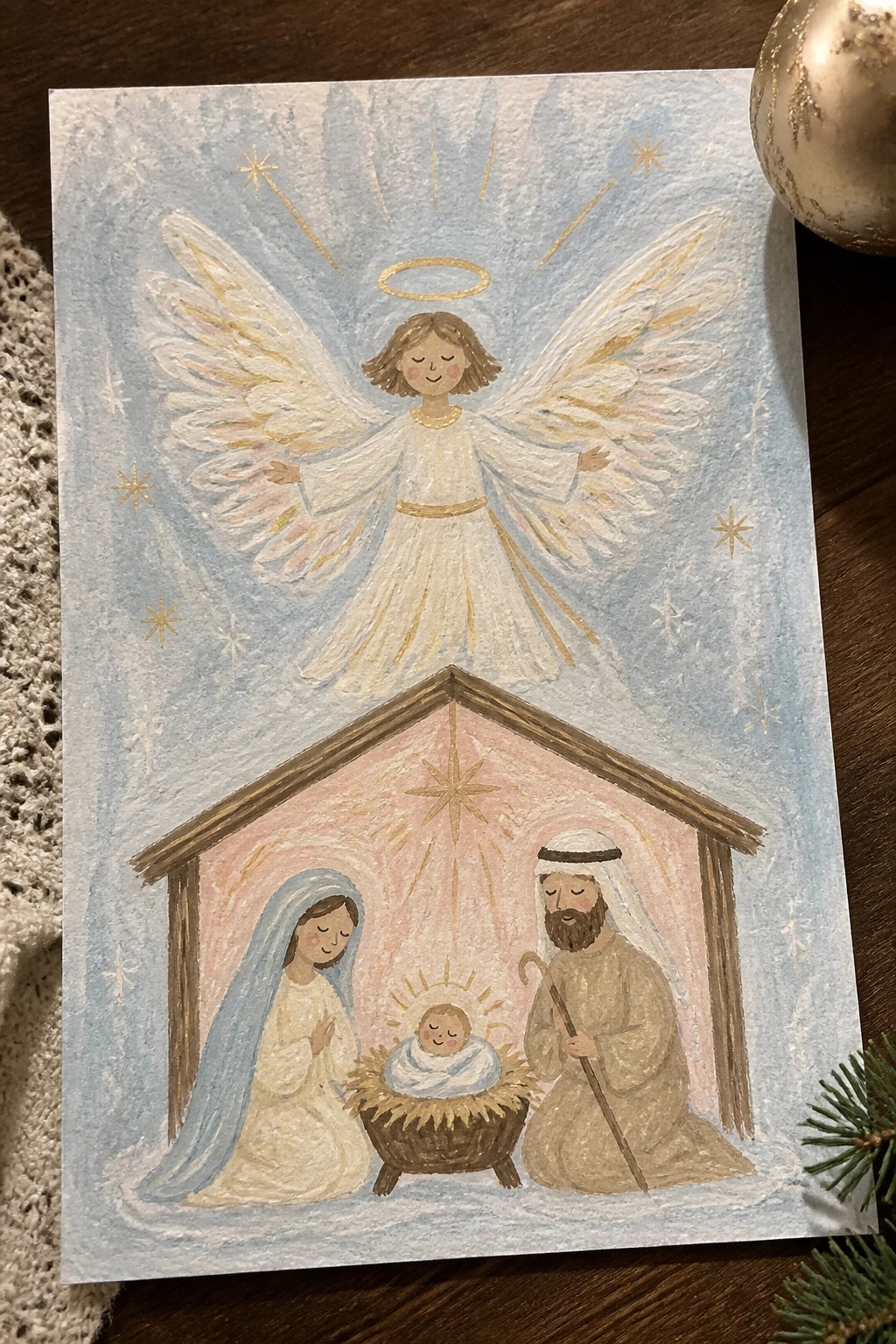 Watercolor nativity with angel above Mary in blue veil, Joseph, and swaddled baby in manger