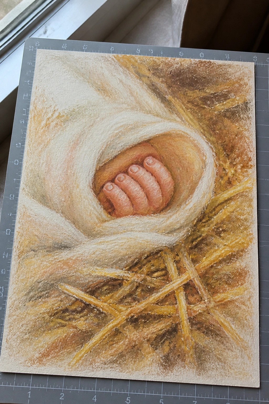 Pastel drawing of a newborn's curled hand emerging from white fabric over straw.
