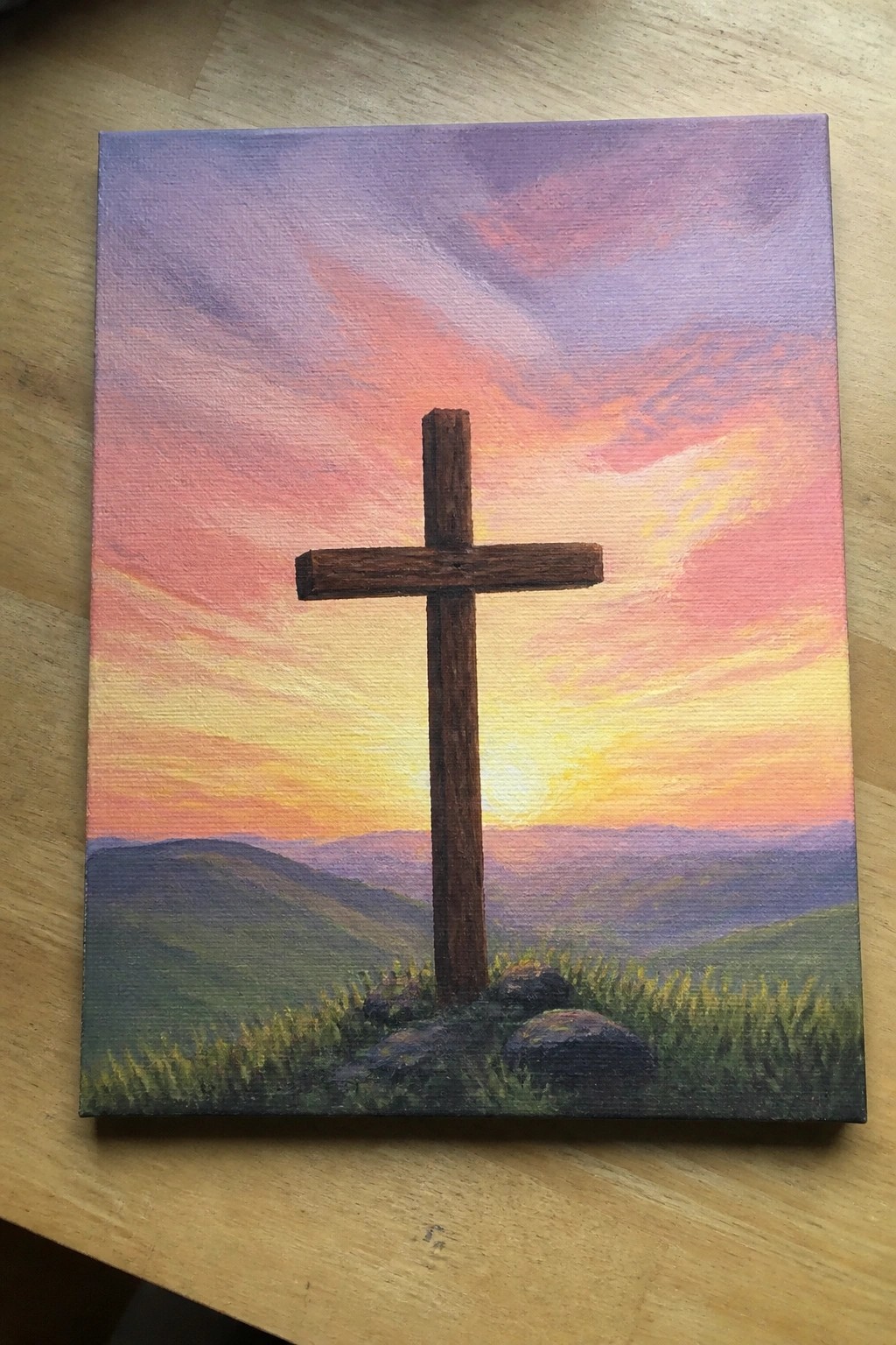 Wooden cross amid grass and rocks with colorful sunset over mountains