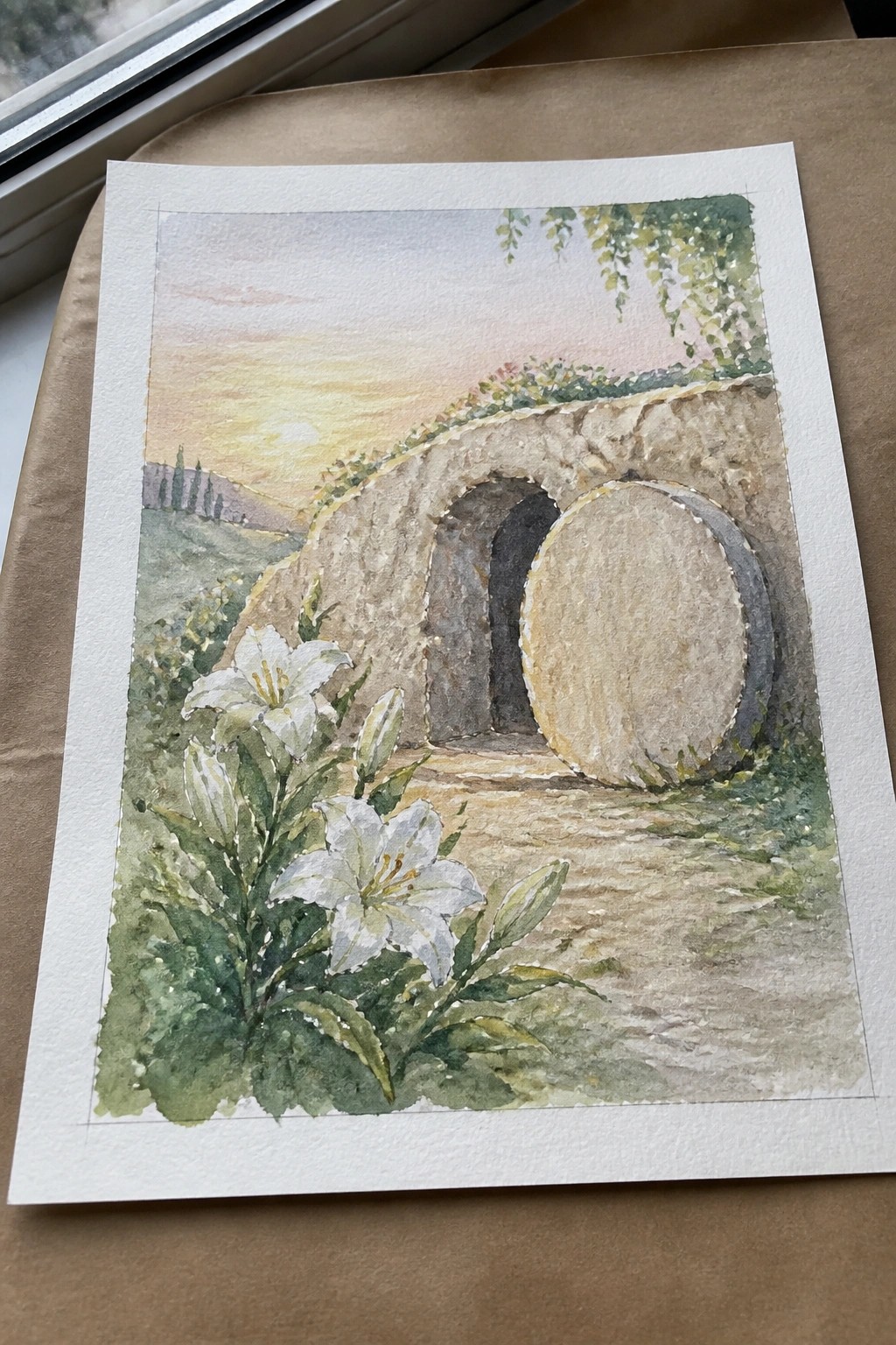 Watercolor of stone tomb with rolled-away circular door, white lilies, and sunset hills