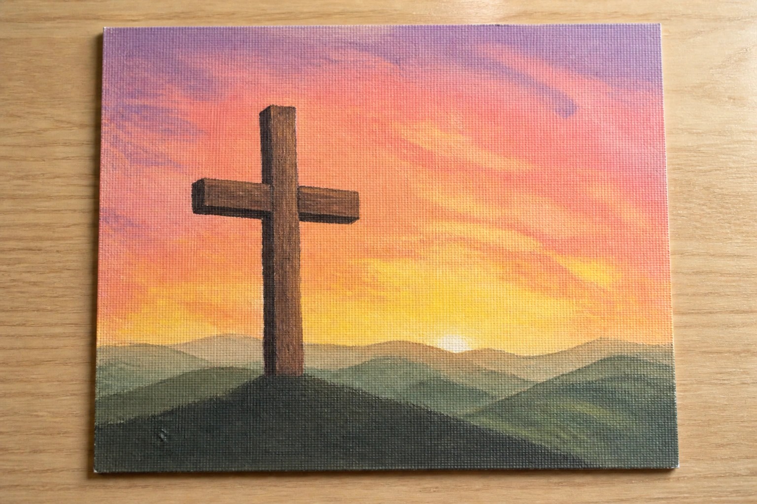 Wooden cross amid grass and rocks with colorful sunset over mountains