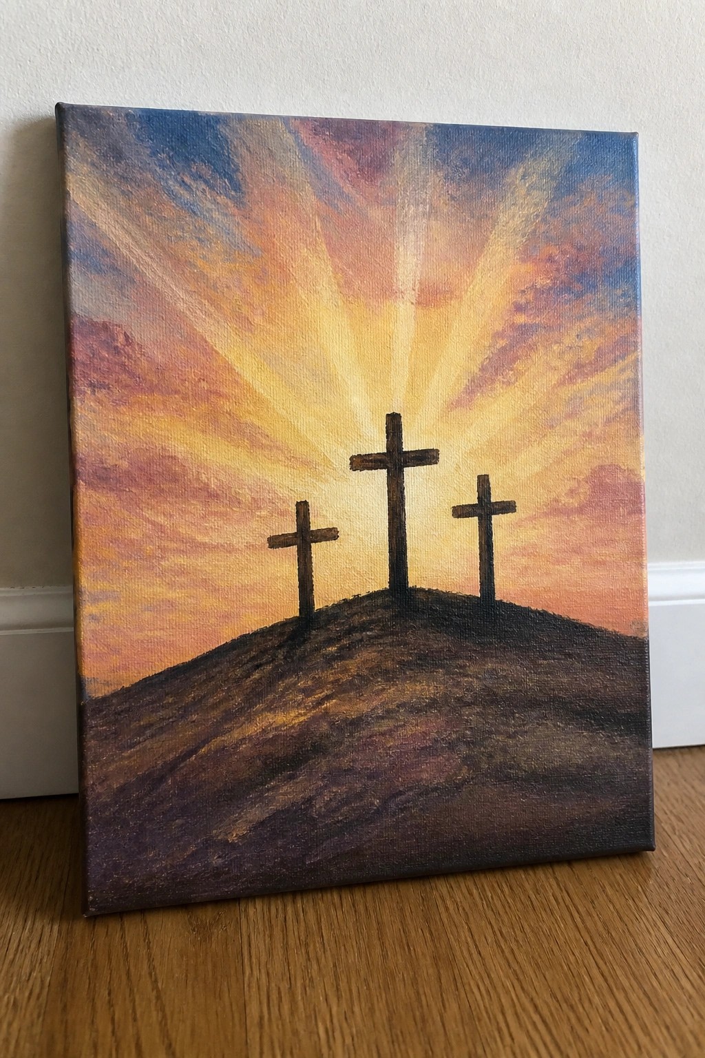 Three crosses on a hill under vibrant sunset sky with golden light rays.