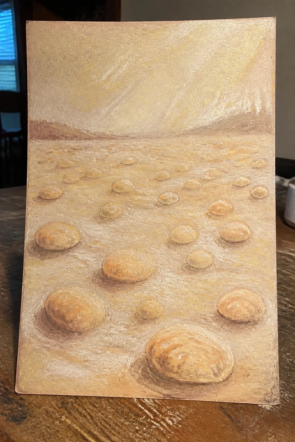 Multiple smooth rounded stones rest on textured sandy ground under a hazy sky.