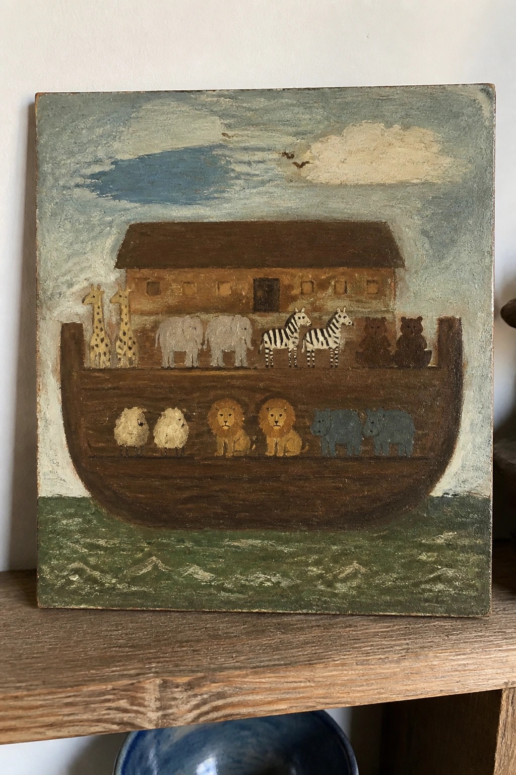 Folk art painting of Noah's Ark with paired giraffes, elephants, zebras, lions, and rhinos on a wooden boat.