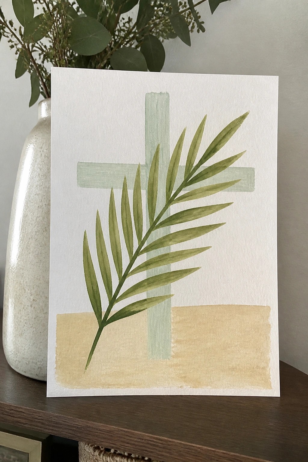 Watercolor cross and palm frond over beige band on white paper