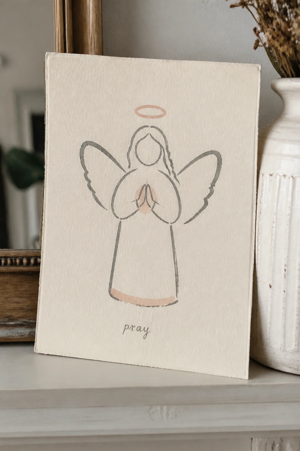 Minimalist line drawing of praying angel with halo on beige canvas beside vase
