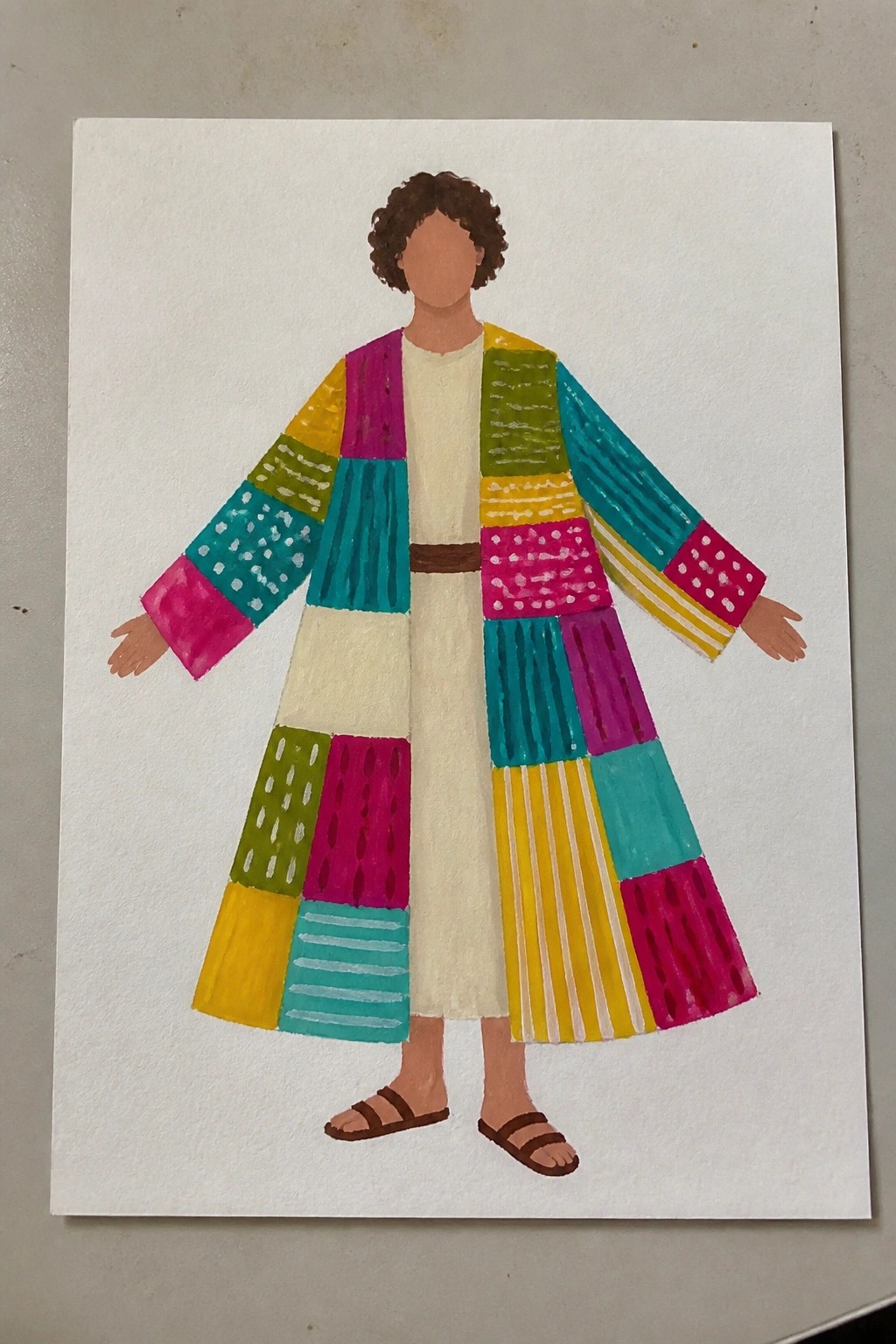 Watercolor of curly-haired figure in vibrant patchwork coat with patterns, white tunic and sandals.