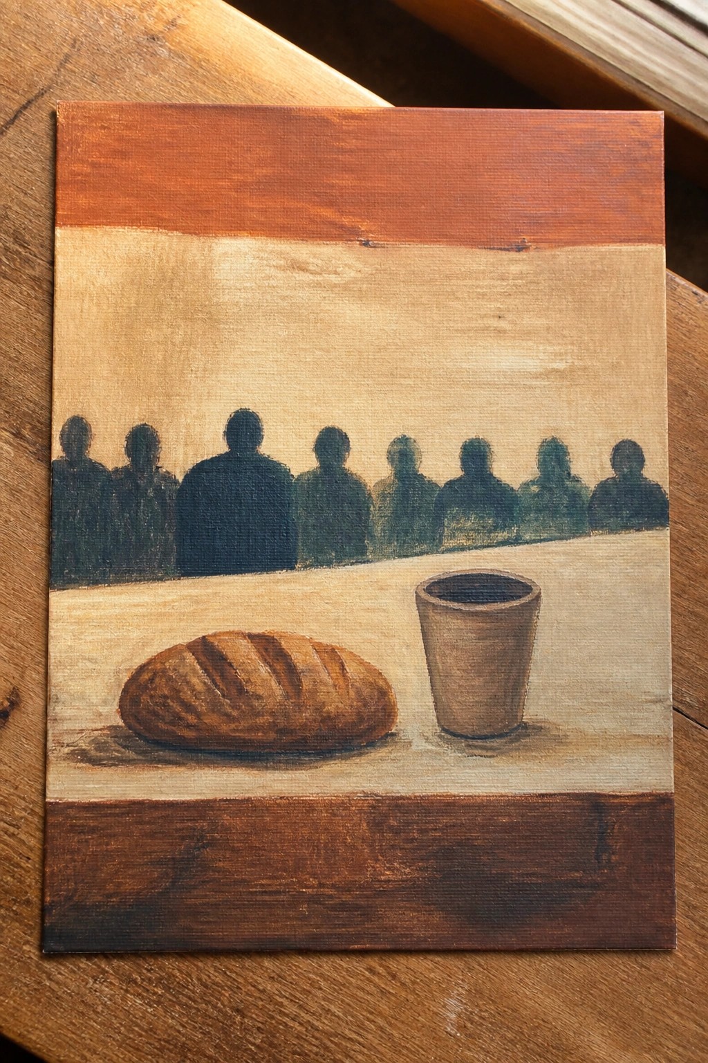 Painting of bread loaf and cup with row of dark silhouetted figures in background