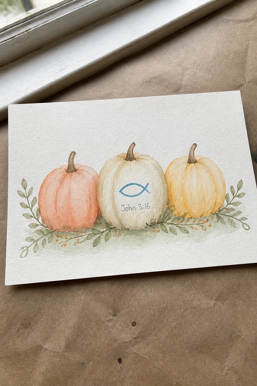 Watercolor of coral, white, and yellow pumpkins with fish symbol and verse on leaves