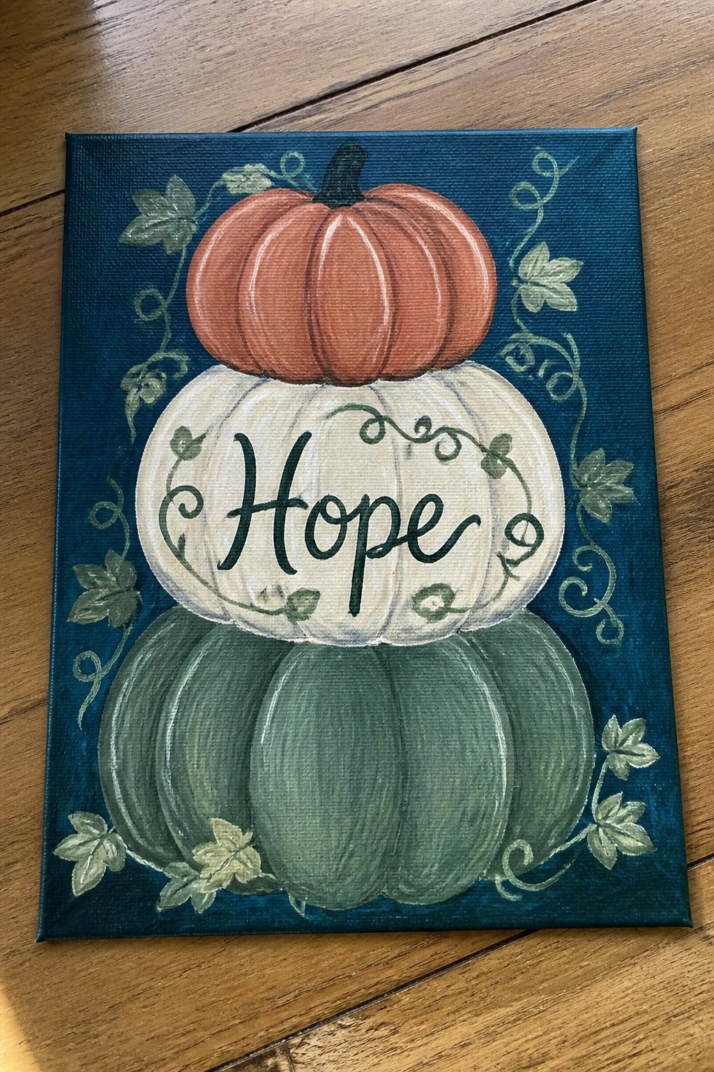 Stacked orange, white, and green pumpkins on blue canvas with Hope text and ivy