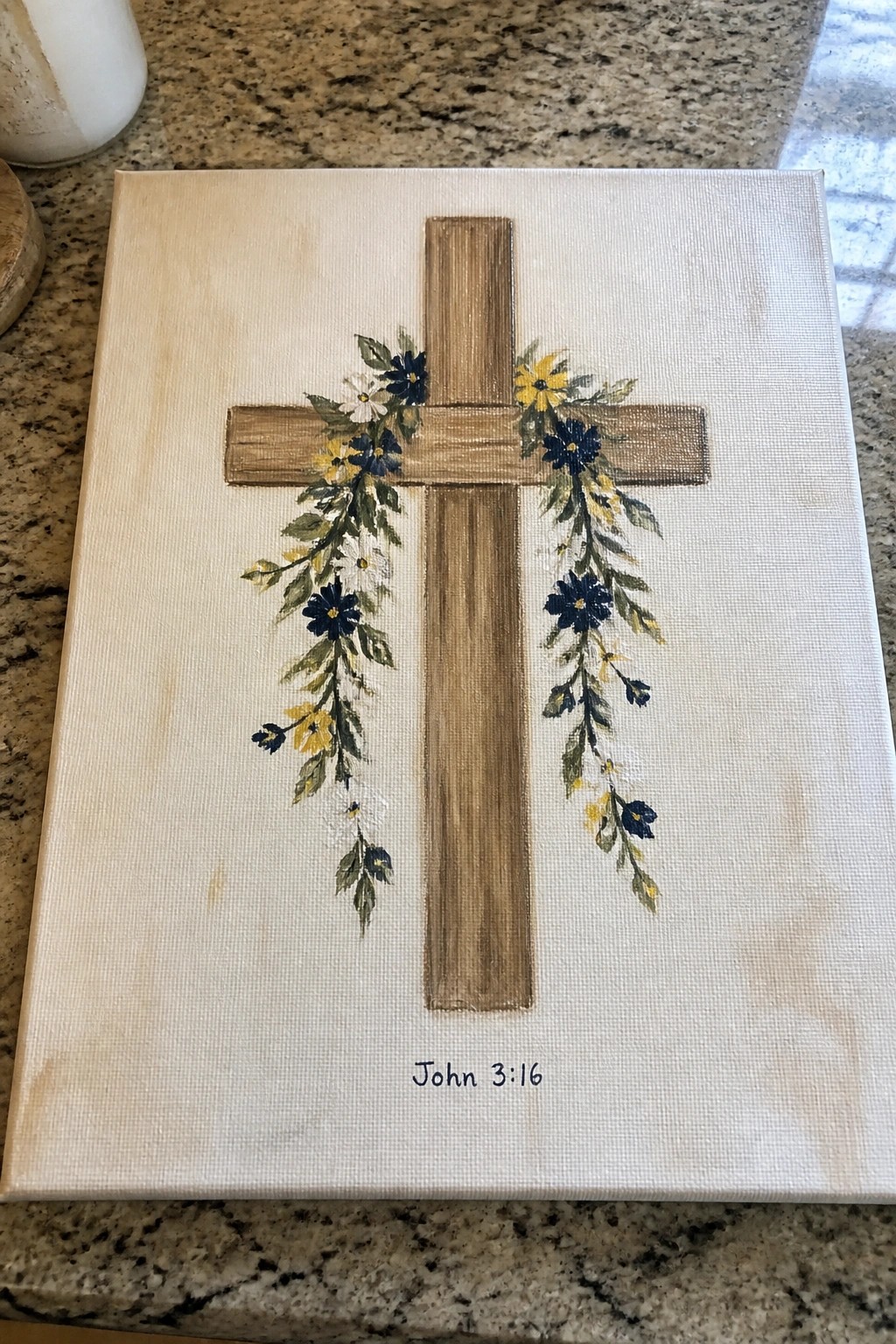 Wooden cross with blue yellow flowers on canvas, John 3:16 below.