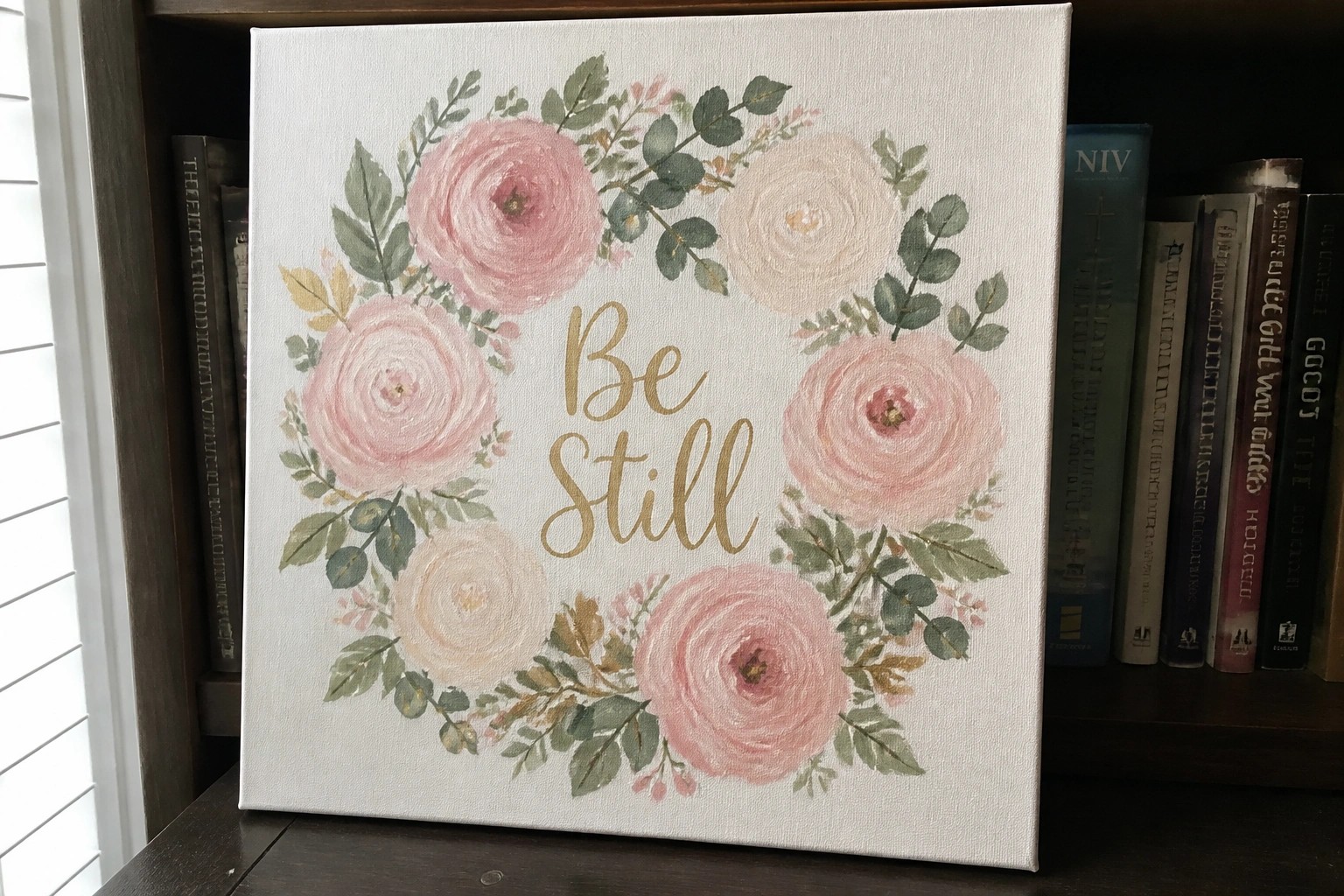 Canvas painting with pink roses, green leaves, and gold "Be Still" text