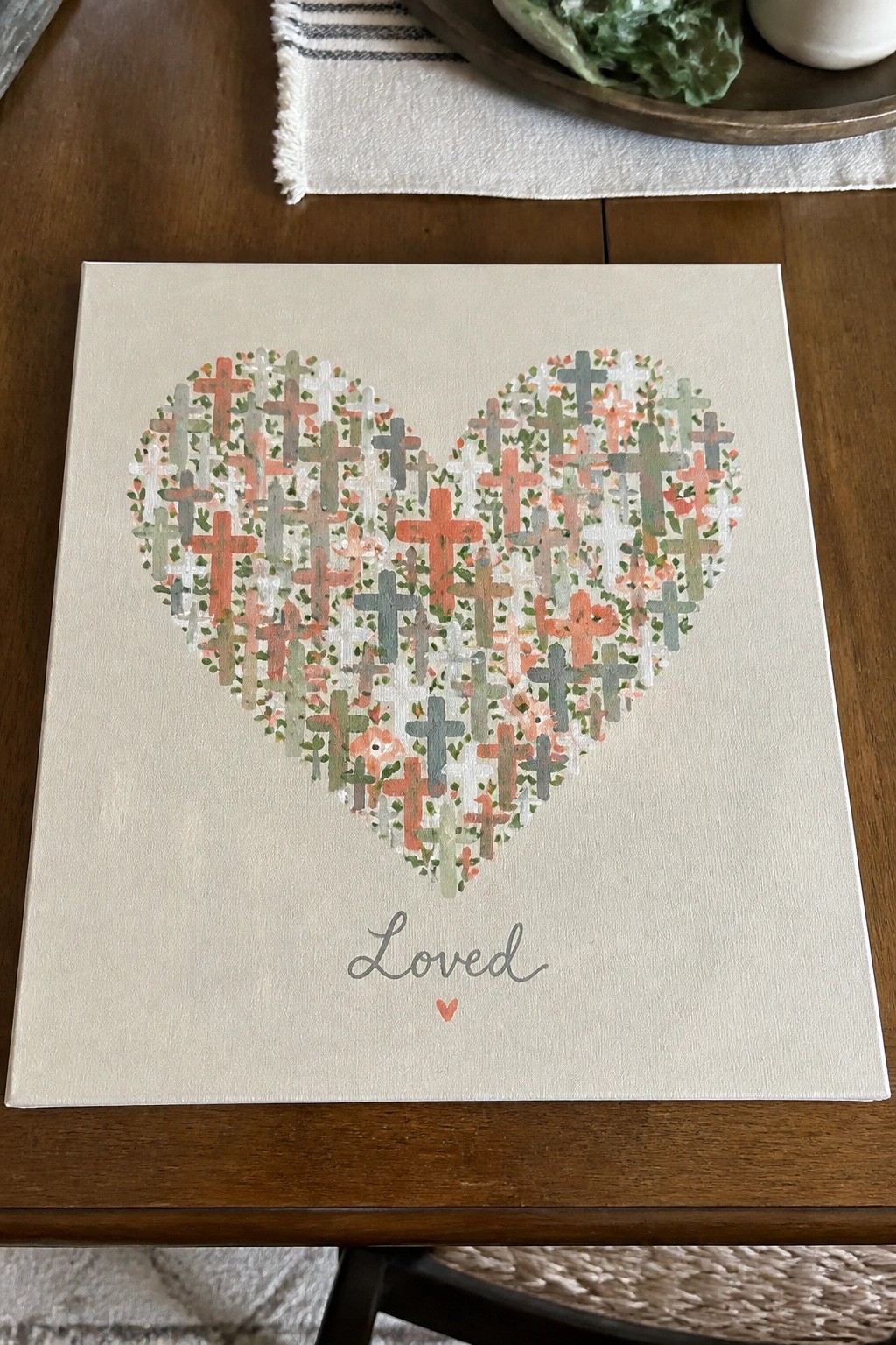 Heart made of colorful crosses above cursive word Loved on beige canvas painting