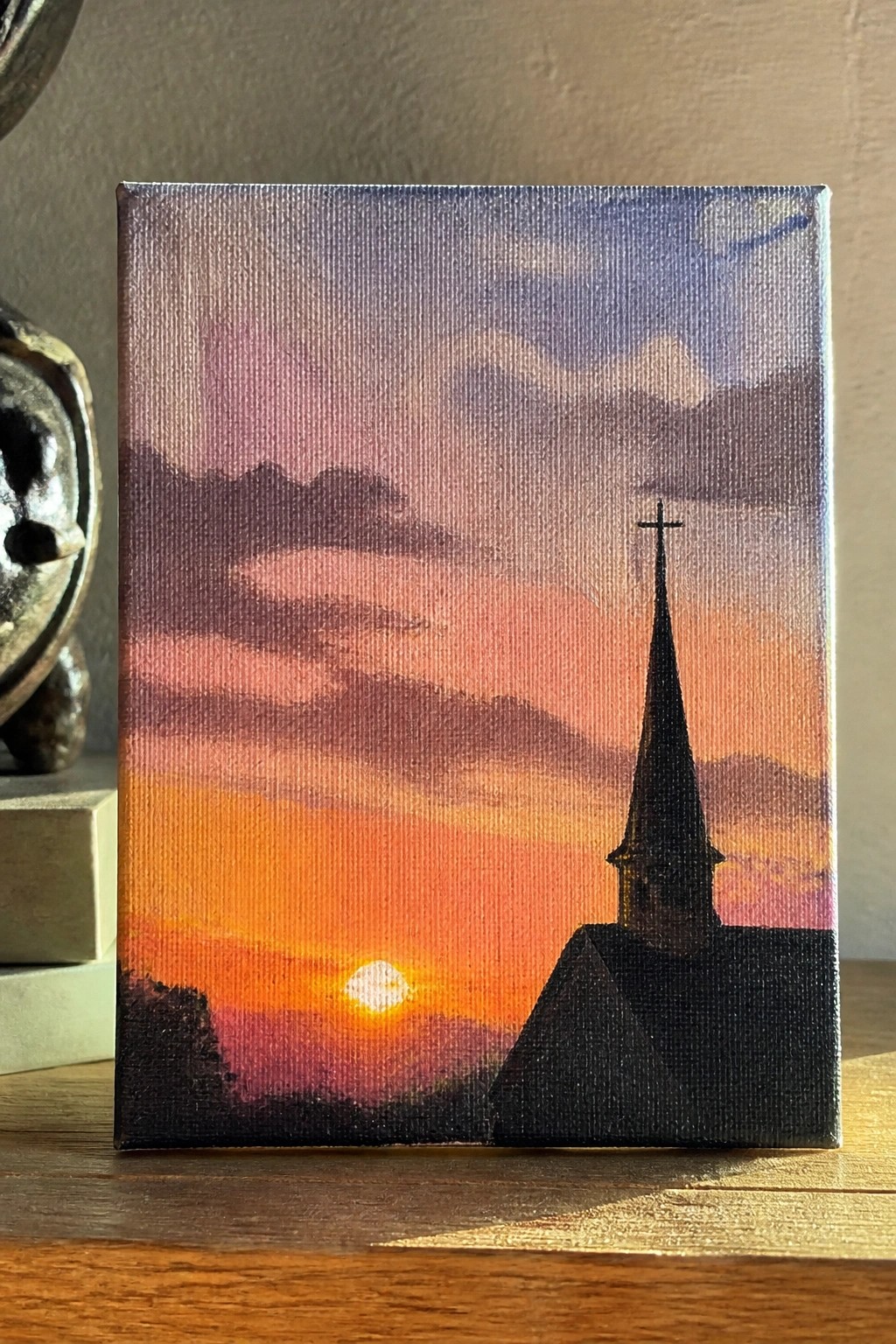 A small canvas shows a black church steeple with a cross silhouetted against an orange-pink sunset sky with clouds and hills.