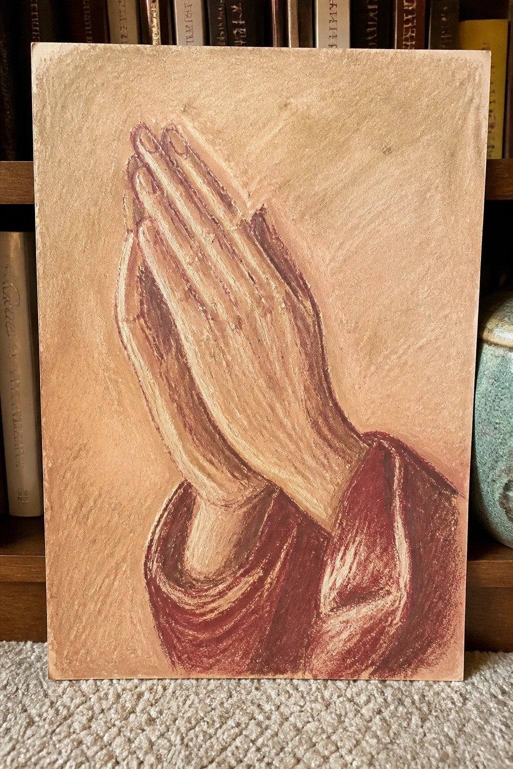 Painting of clasped hands in prayer with maroon sleeves on beige background