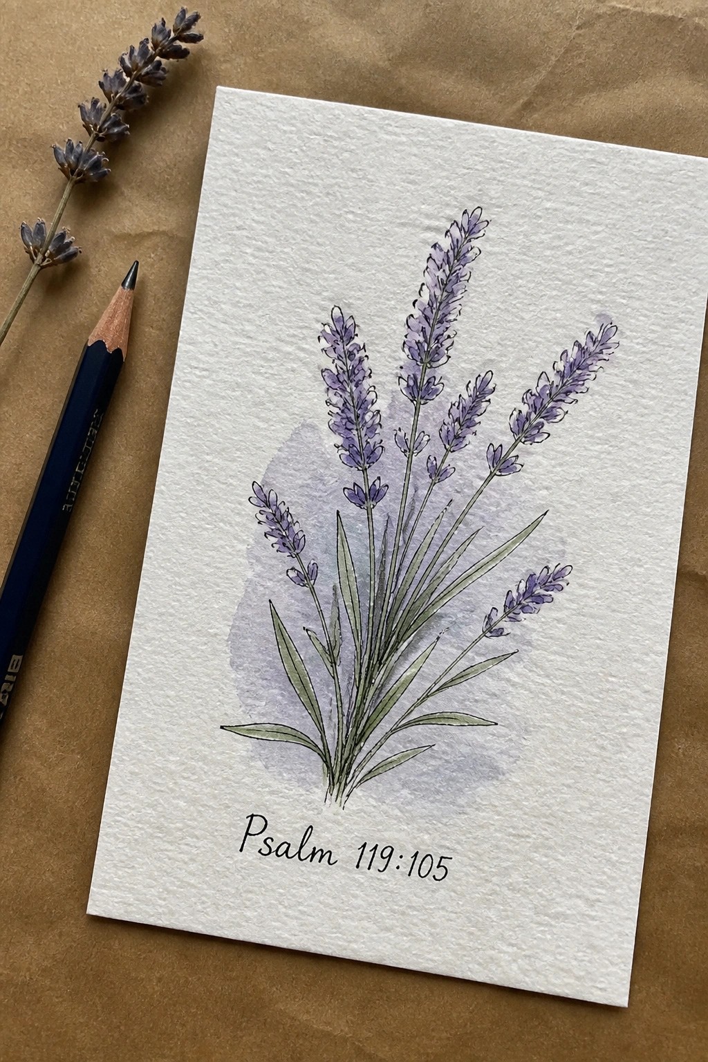 Watercolor lavender stems with Psalm 119:105 on white paper beside blue pencil and dried sprig