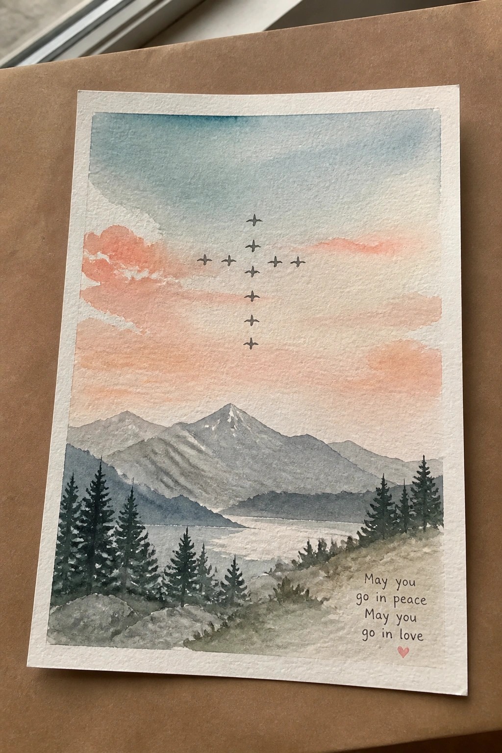 A watercolor landscape shows mountains and a lake at sunset with birds arranged in a cross shape in the sky and text at the bottom reading 
