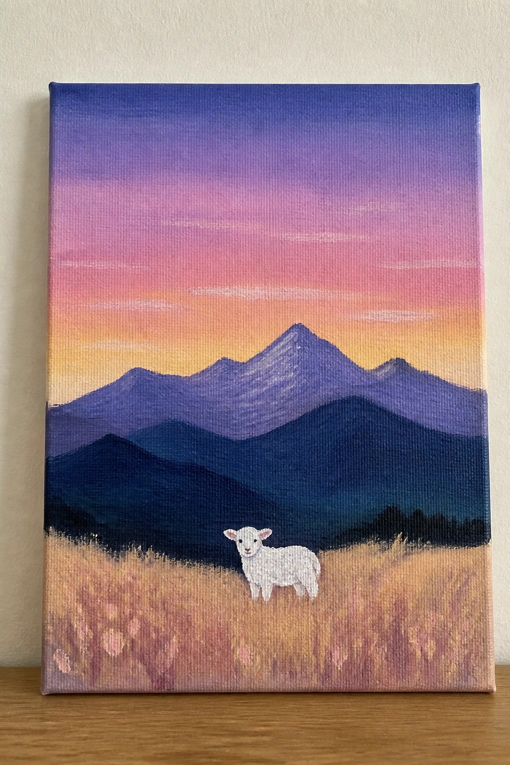 White lamb stands in golden field before layered purple mountains at sunset.