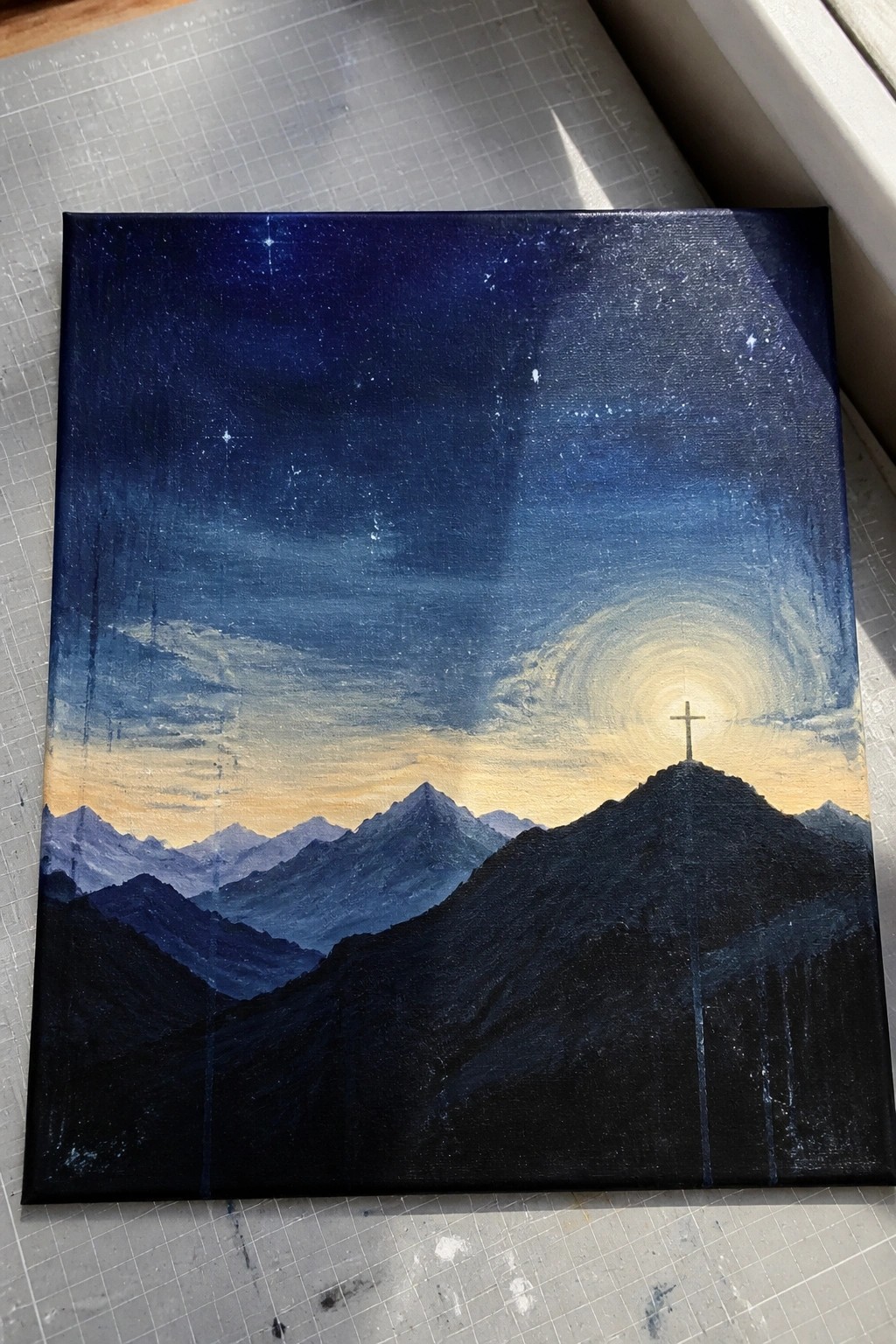 Starry night sky painting over silhouetted mountains with glowing cross on peak