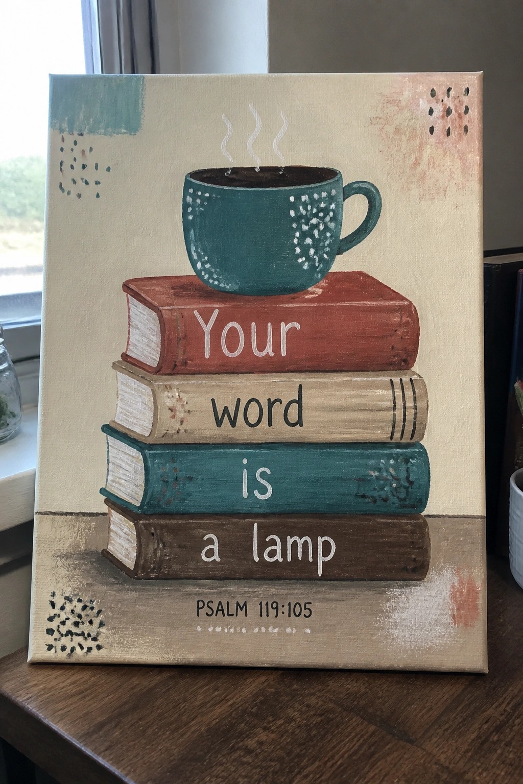 A canvas shows a stack of four books with a teal mug on top and the verse 