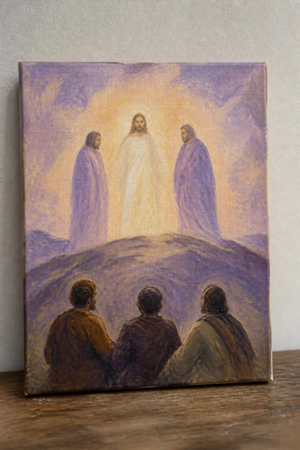A painting shows Jesus glowing in white on a hill with two robed figures beside him and three men seated in the foreground.