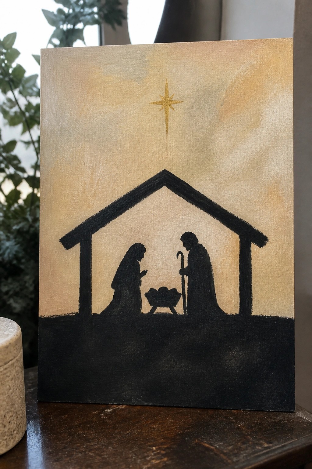 Black silhouette nativity with robed Mary, Joseph, manger, and golden star on canvas