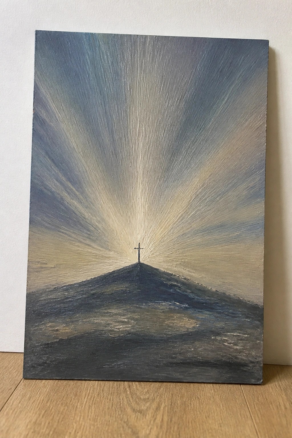 Painting of cross atop dark hill with light rays radiating into blue-gray sky.