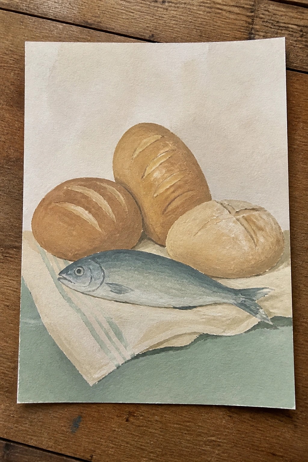 Watercolor still life of three bread loaves and a fish on striped cloth
