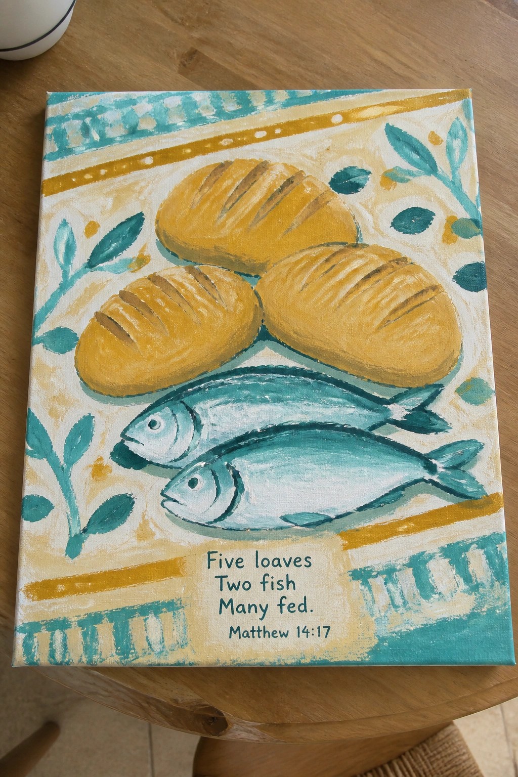 Folk art canvas painting of three loaves, two fish, and biblical verse text