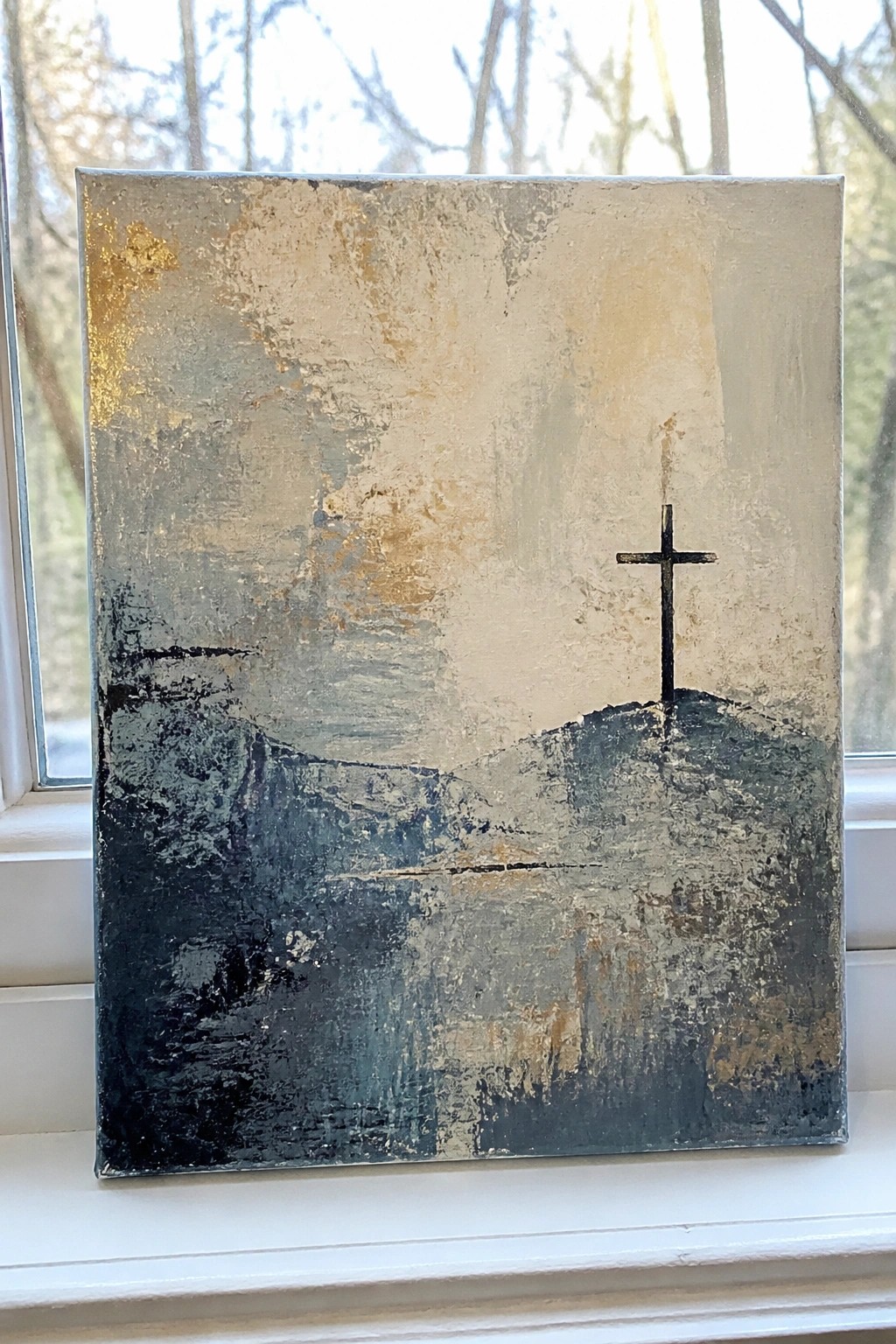 Abstract painting with black cross on textured hill, gold and blue tones on windowsill.