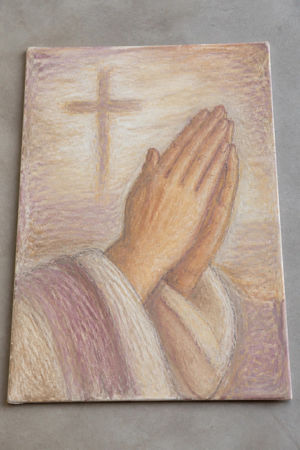 Clasped praying hands with faint cross on soft pastel background