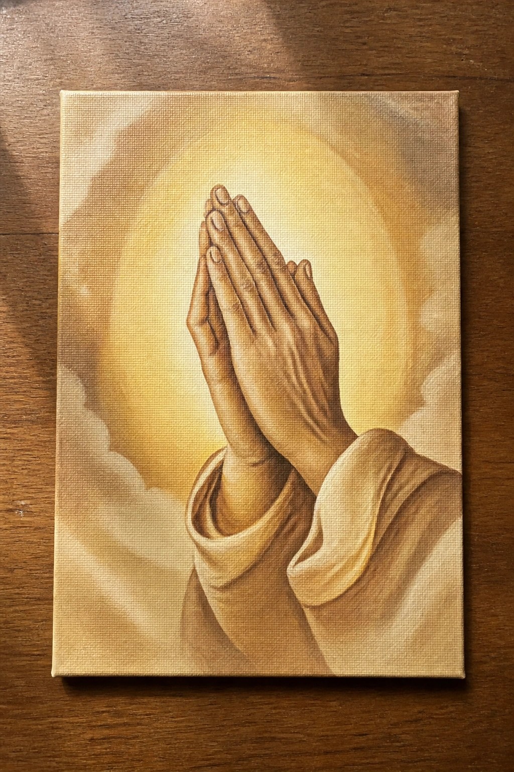 Praying hands in beige sleeves before a radiant golden cloudy glow on canvas