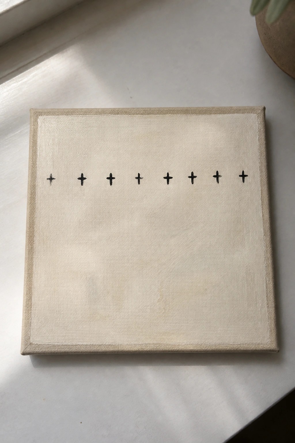 Beige canvas on white surface with centered row of black crosses.