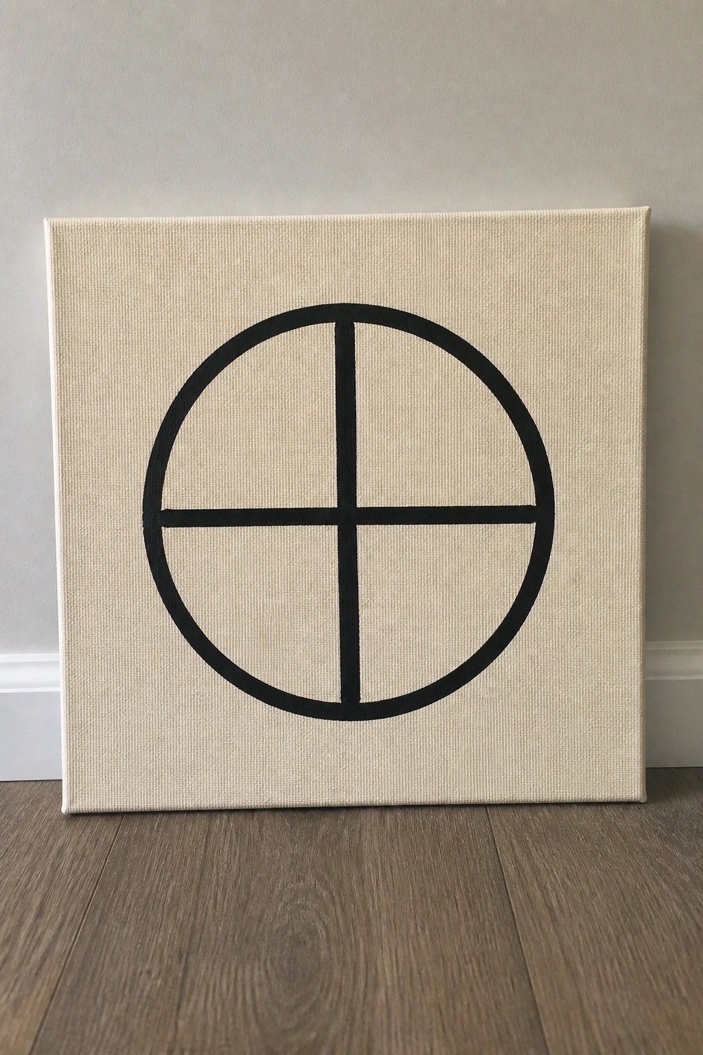 Square beige canvas with black circle and cross on wooden floor against wall