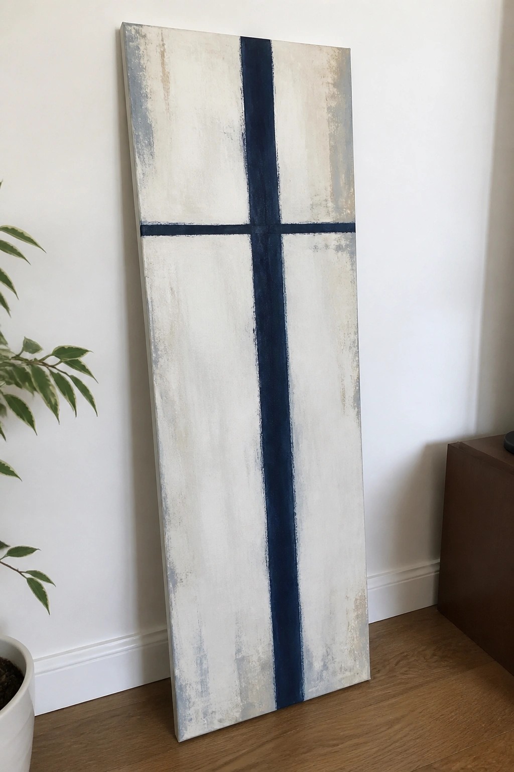 Tall abstract painting with dark blue cross on textured white background leaning on wall