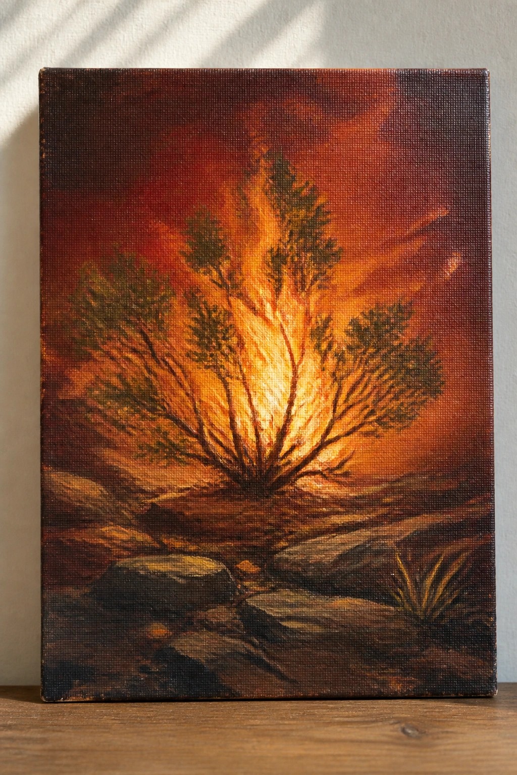 Dramatic painting of a blazing tree with orange flames against red sky and rocky ground.