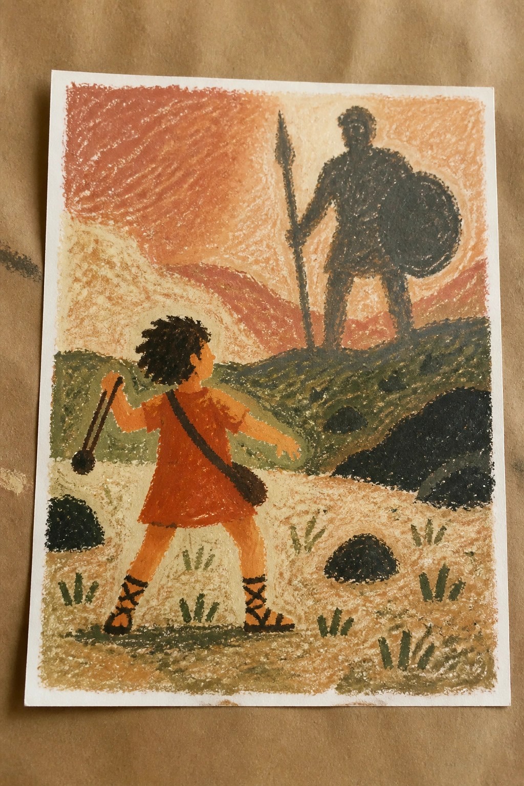 Young figure in orange tunic with slingshot faces dark warrior on sunset hill