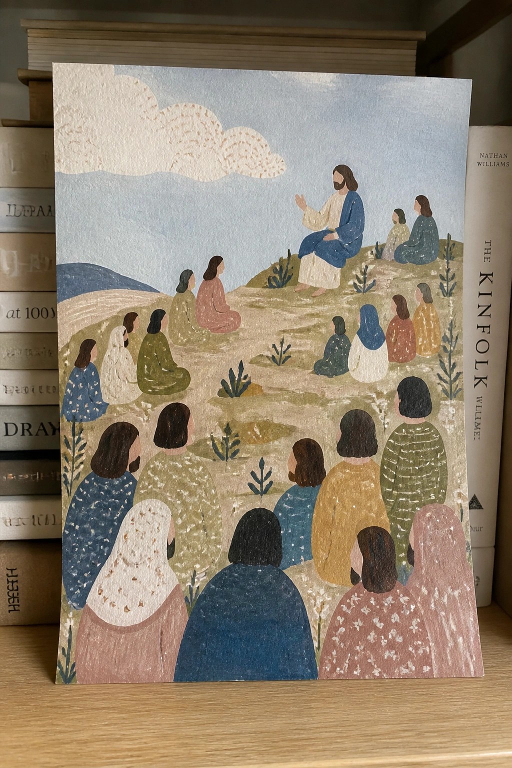 Jesus in blue robe teaches seated crowd in colorful robes on grassy hillside.