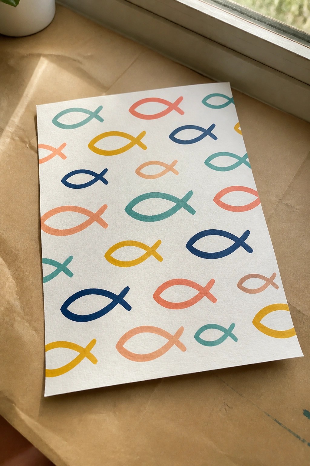 White paper with colorful fish symbols on brown surface by window