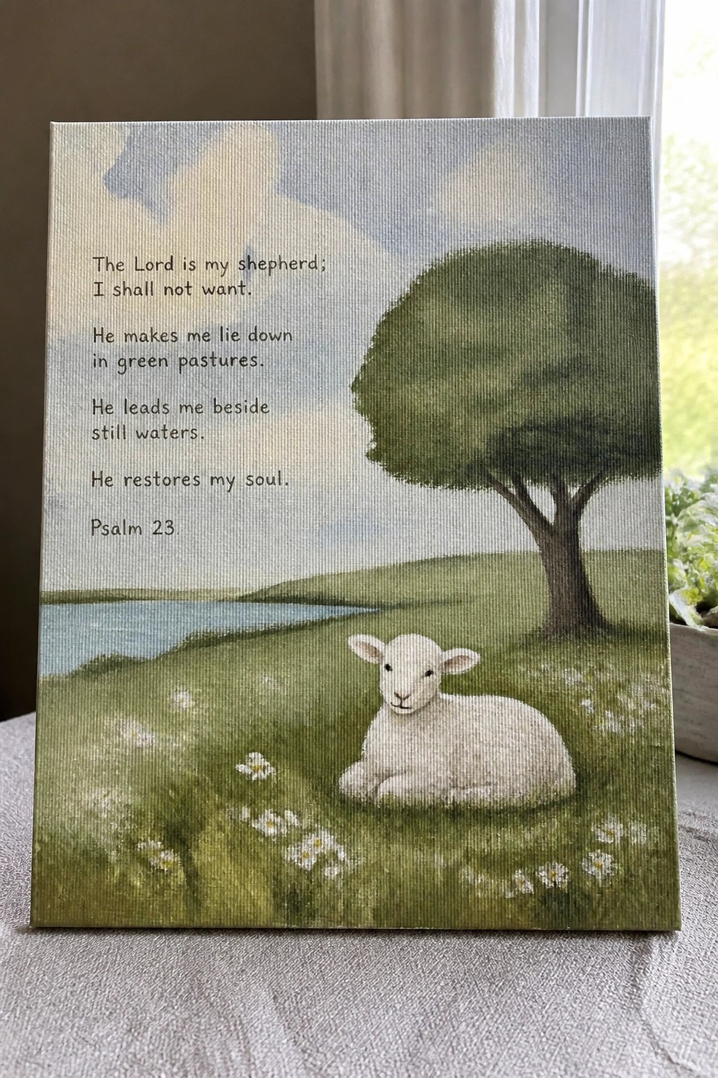 Canvas with Psalm 23 text and white lamb resting in green field by tree and stream.
