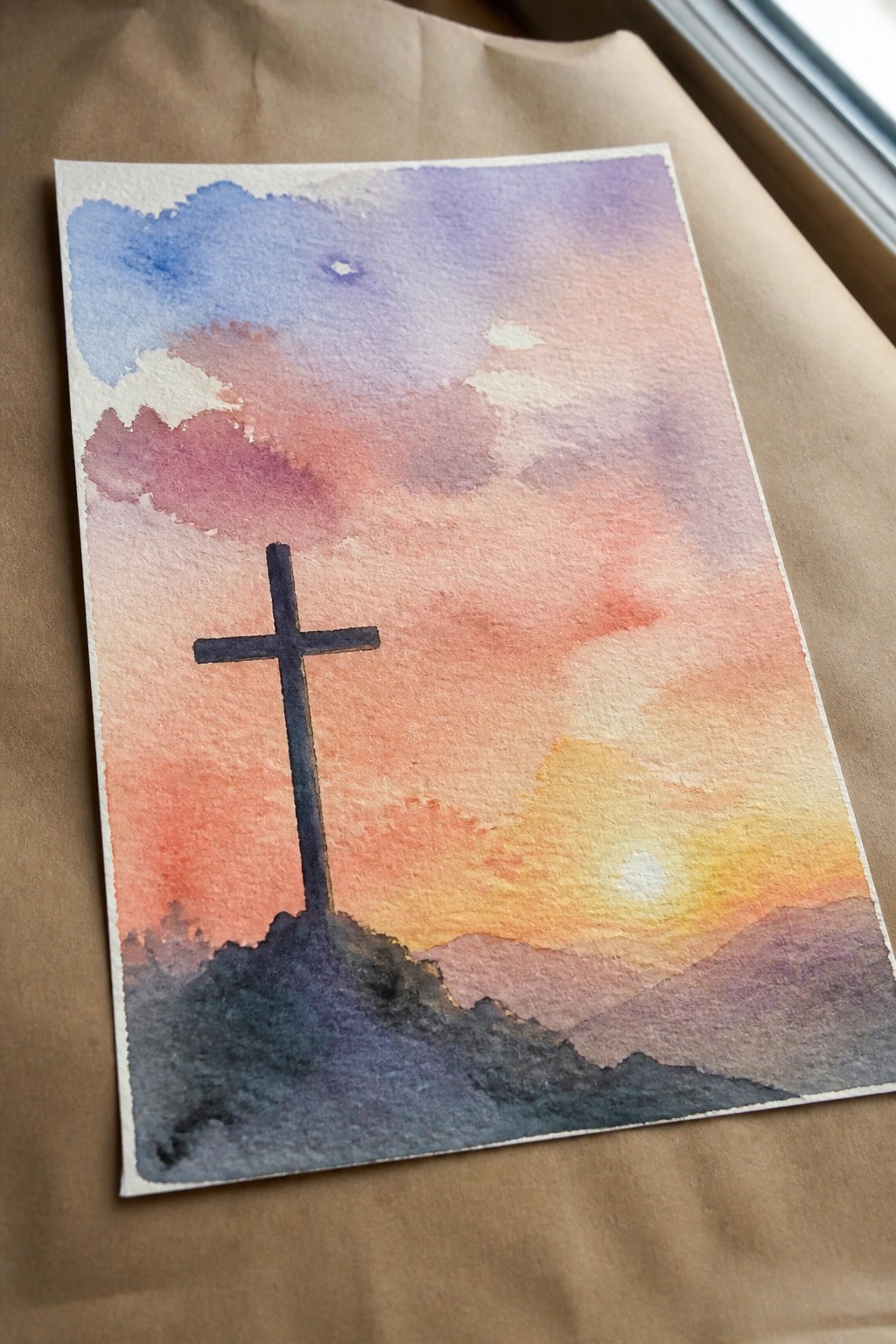 Watercolor sunset painting with silhouetted cross on dark hill under colorful sky