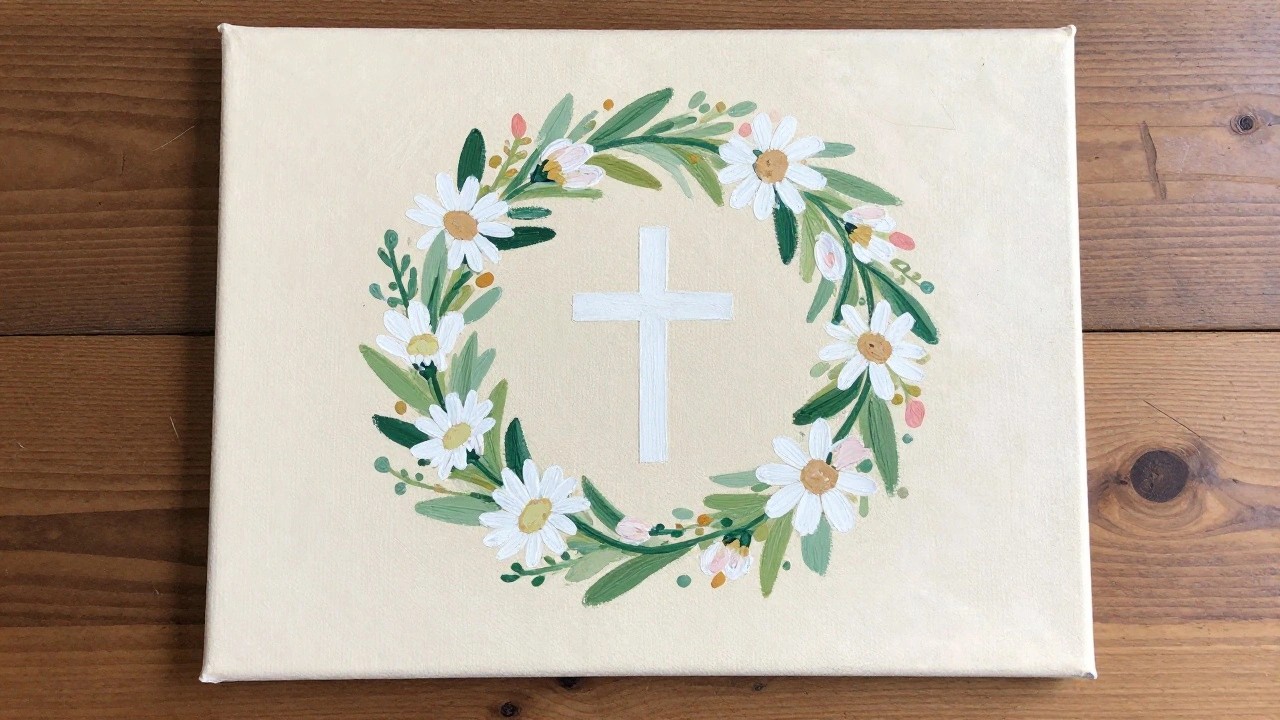 Canvas with daisy wreath encircling white cross on wooden surface