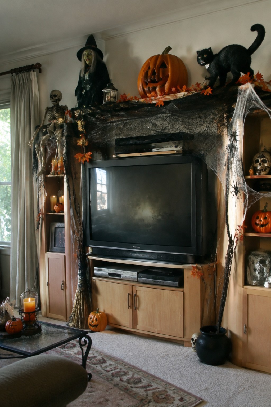 Living room entertainment center covered in fake spiderwebs with a black cat, jack-o'-lantern, and witch figure displayed across the top.