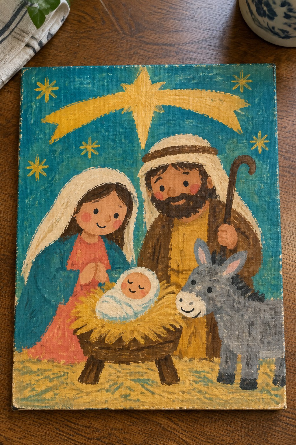 Folk-art nativity painting with Mary in blue cloak, Joseph holding staff, smiling donkey, and bright star.