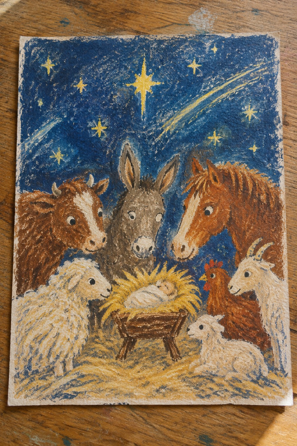 A pastel-style painting shows a baby in a manger surrounded by a cow, donkey, horse, sheep, goat, chicken, and lamb under a dark blue starry sky with a yellow streak.