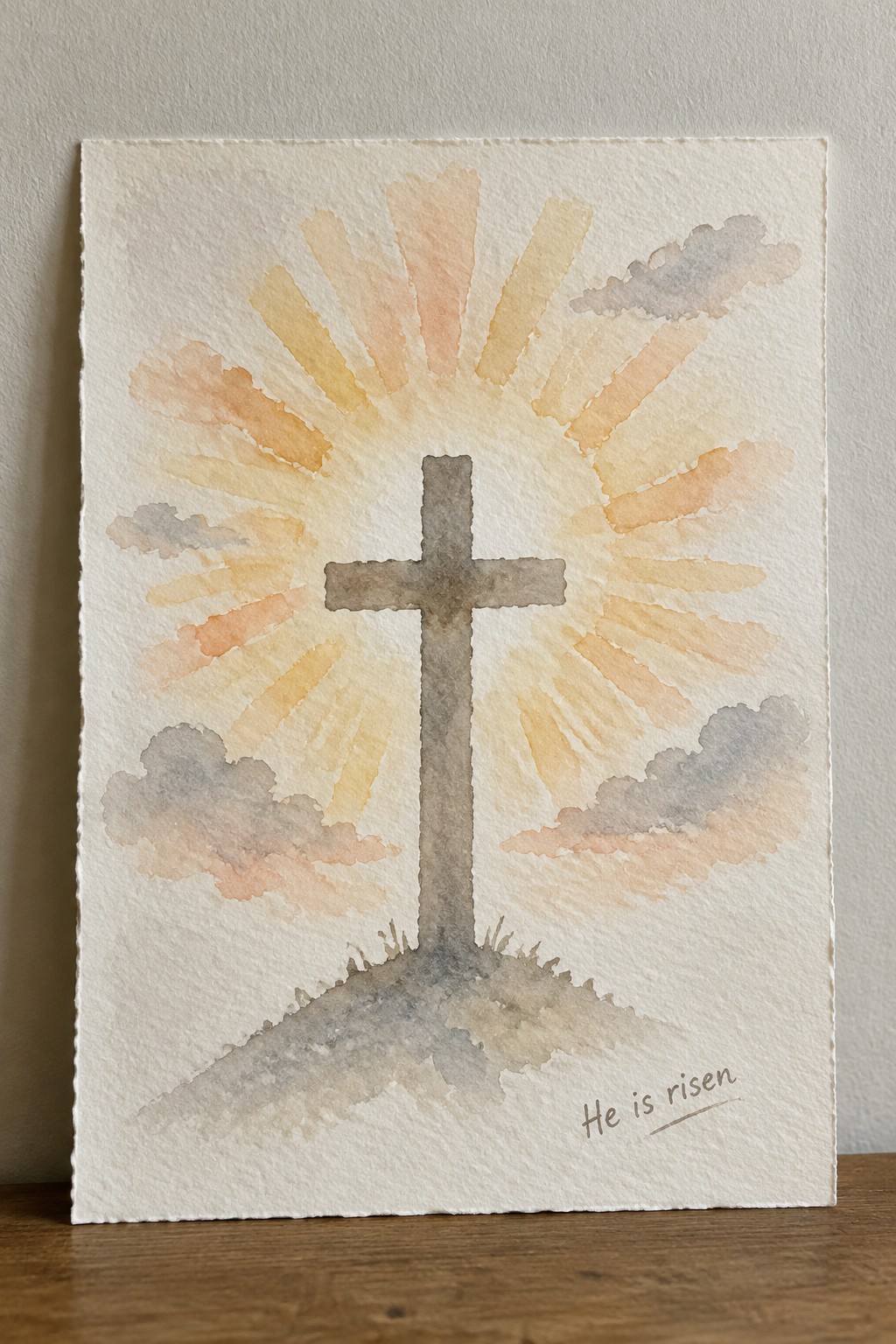A watercolor painting of a brown cross on a hill with orange and yellow sunrise rays, clouds, and the words 