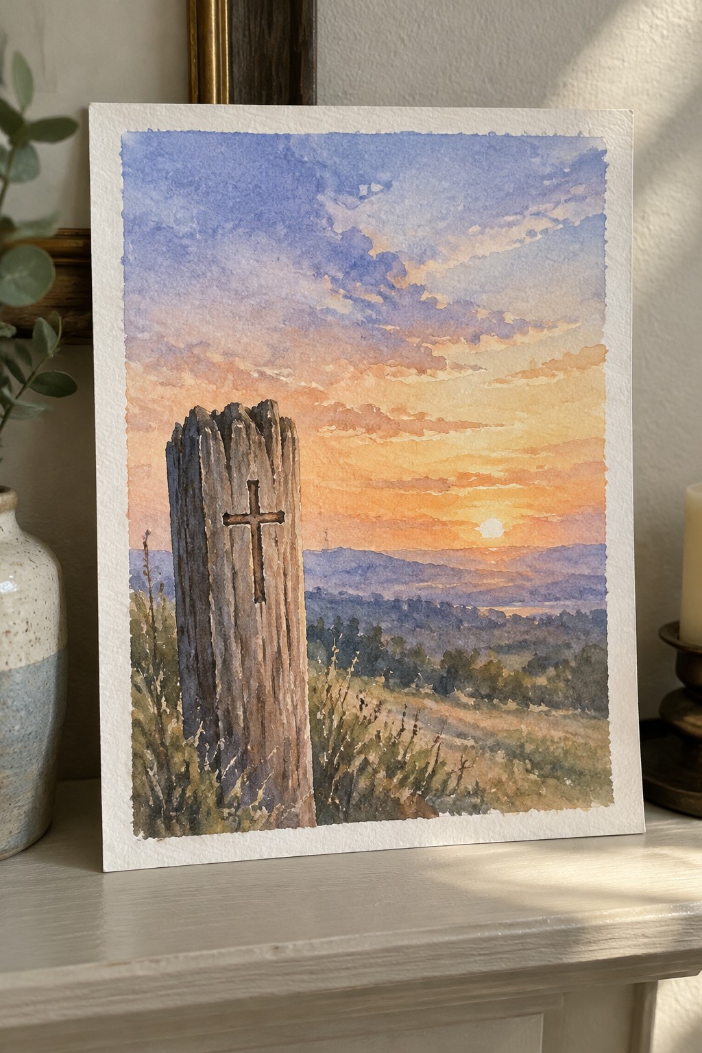 Watercolor painting of weathered wooden cross overlooking vibrant sunset and rolling hills.