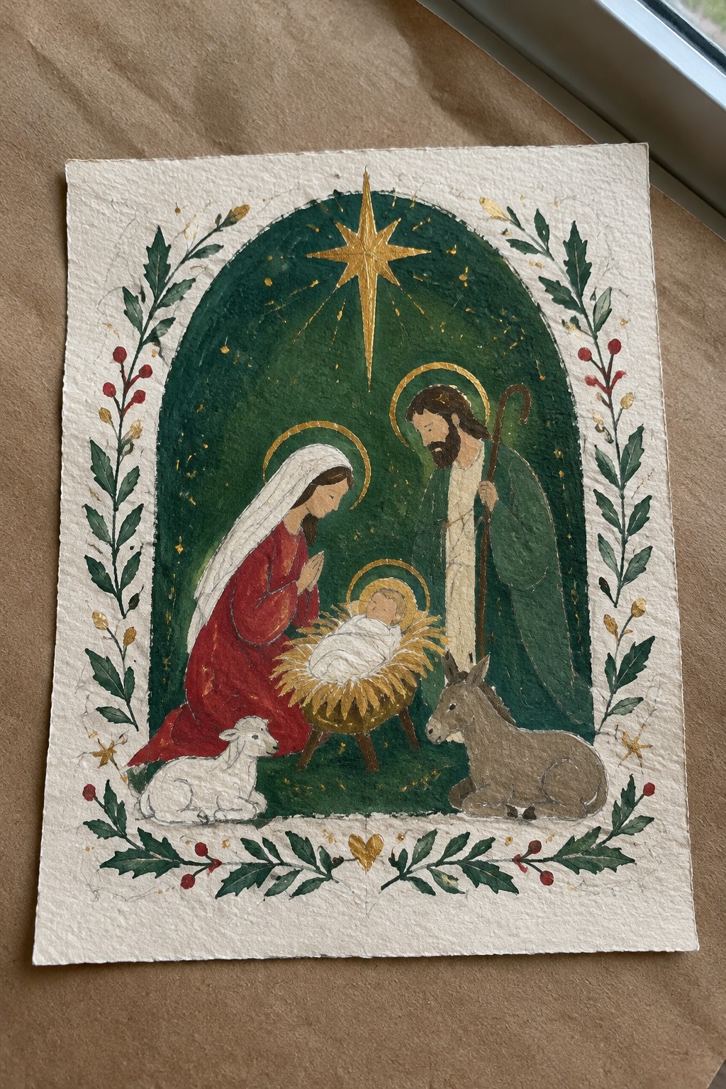 Watercolor nativity with Mary in red veil, Joseph with staff, baby in manger, lamb, donkey under golden star.