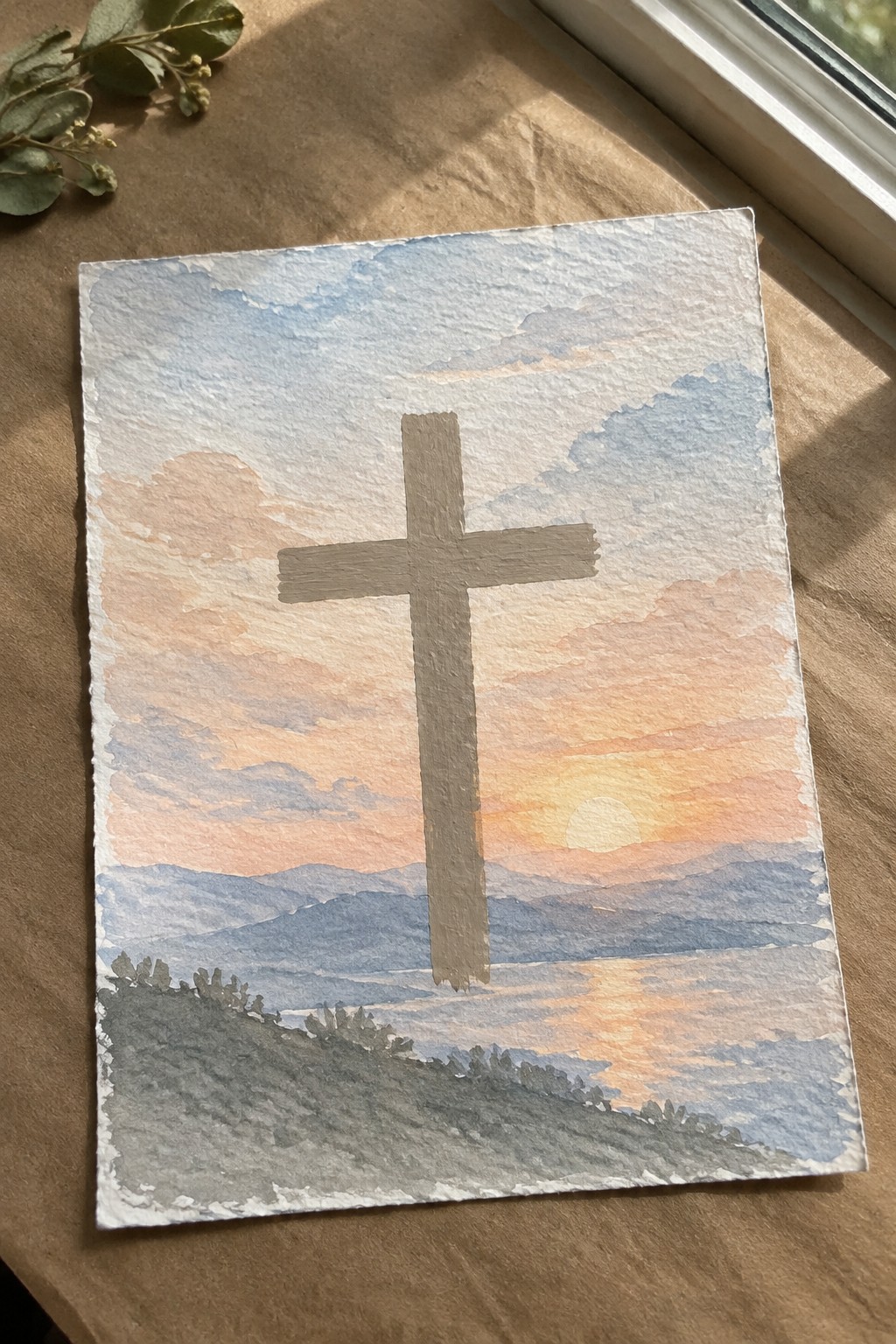 Watercolor painting of a cross overlooking a sunset mountain landscape with clouds