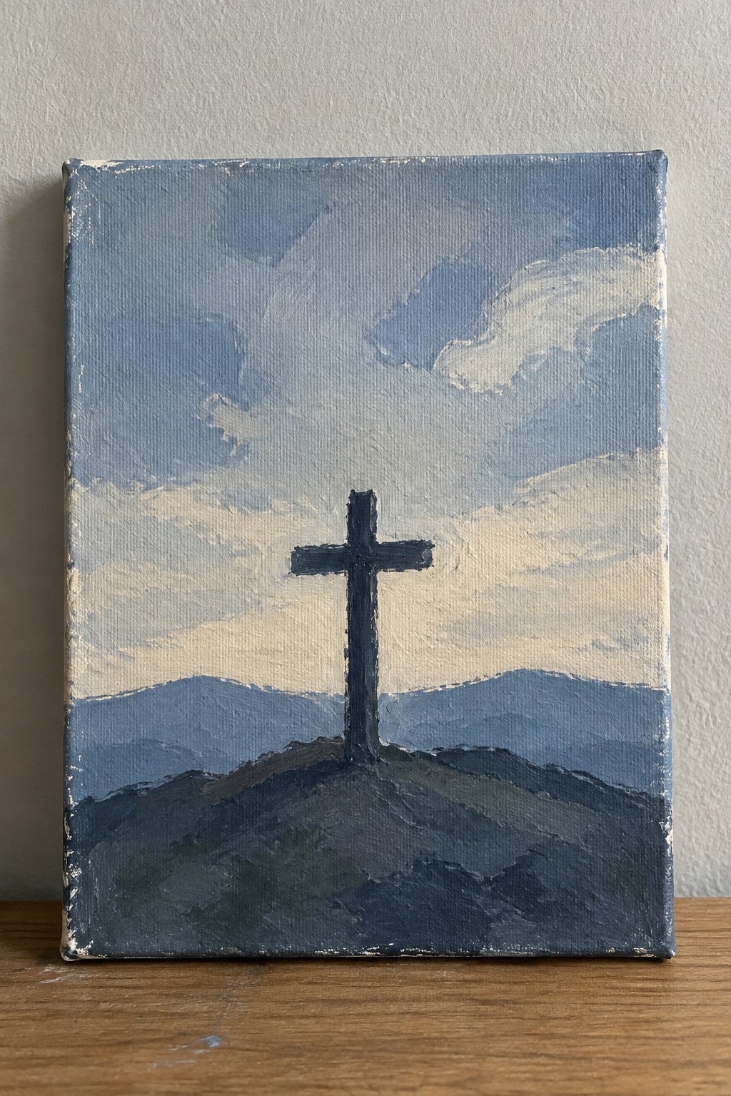 Dark cross on hill under cloudy blue sky with layered mountains in background